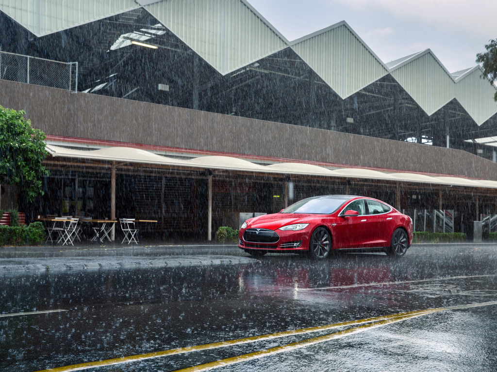 Red car Tesla Model S on the road in the rain