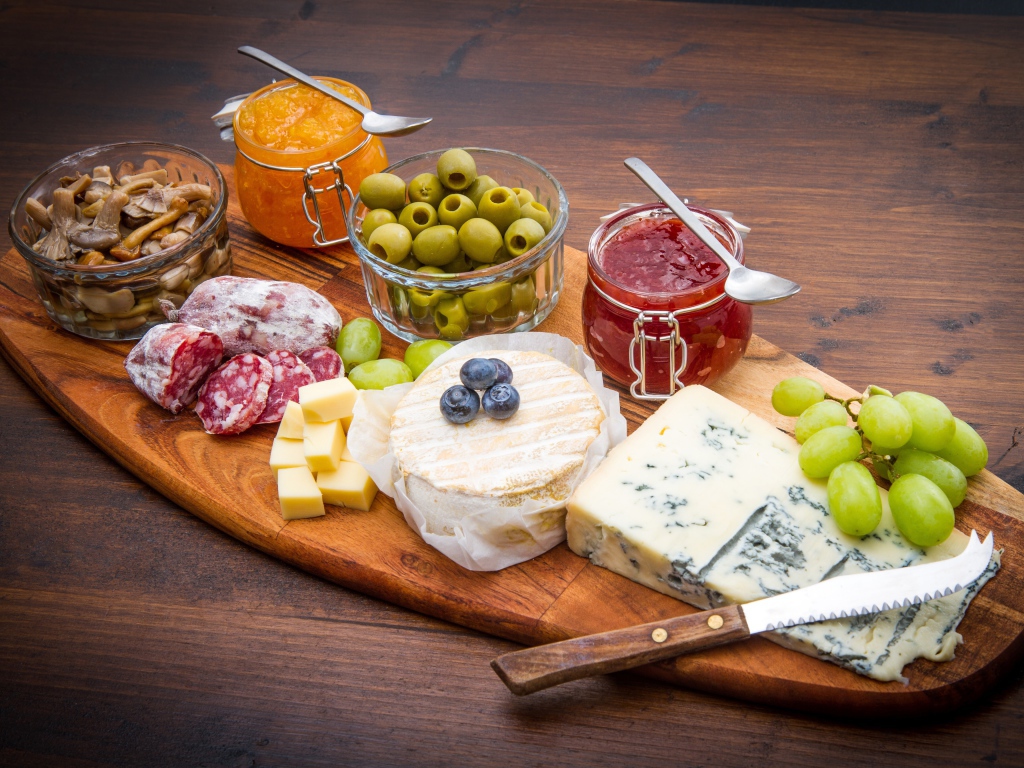 Сыр, грибы, маслины, колбаса, виноград и джем на разделочной доске 