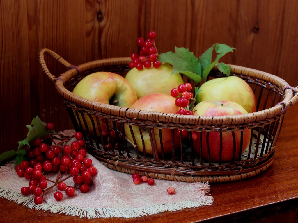 Красивые яблоки в корзине на столе с ягодами калины