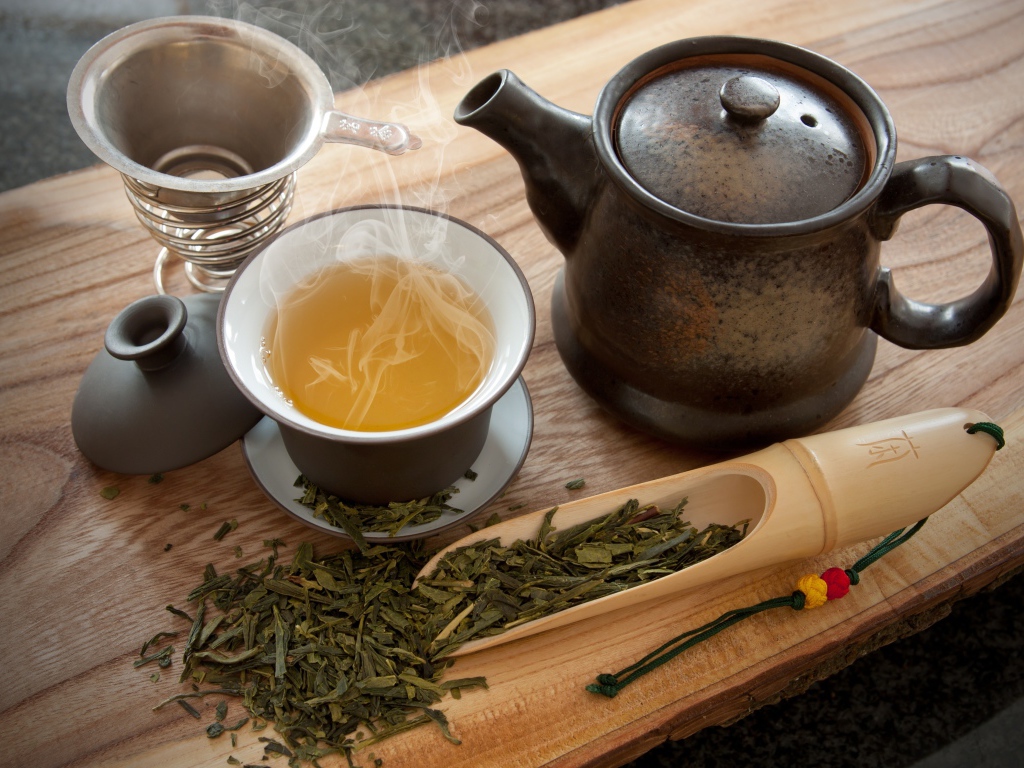 Свежий горячий чай на столе с чайными листьями и чайником