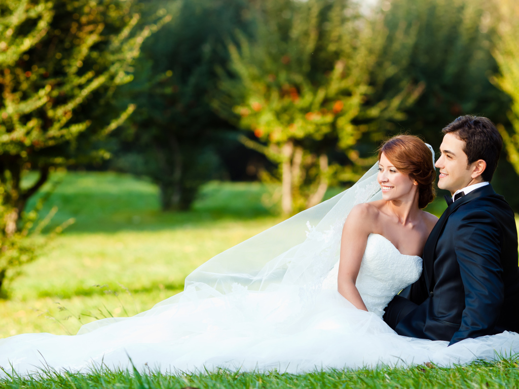 Счастливые жених и невеста сидят на зеленой траве