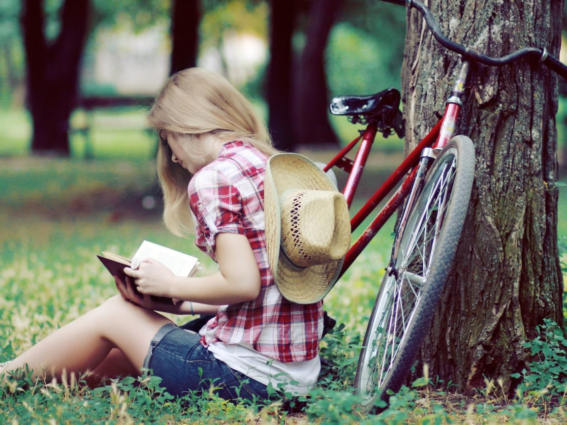 Девушка читает книгу сидя в парке на газоне