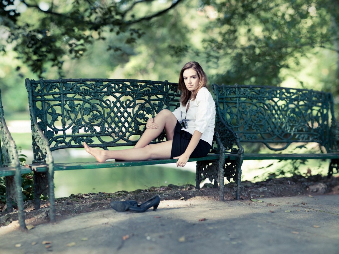 Девушка сидит на кованной парковой скамье