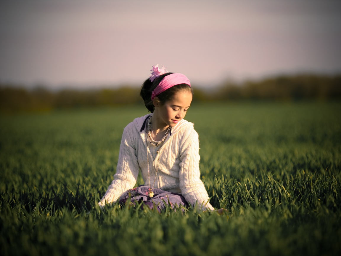 Девочка с розовой повязкой на голове сидит в зеленой траве
