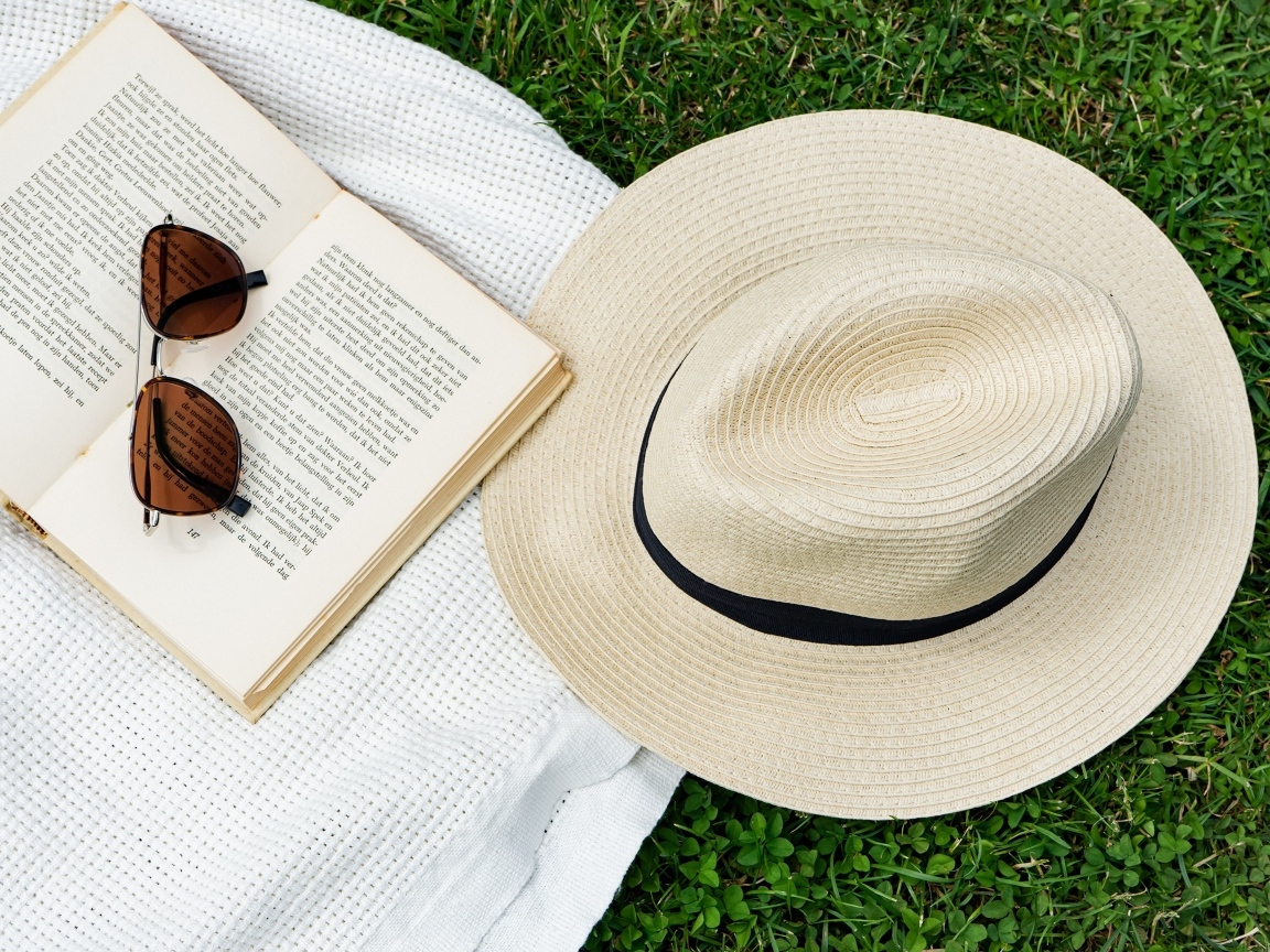 Шляпа лежит на зеленой траве с книгой и очками