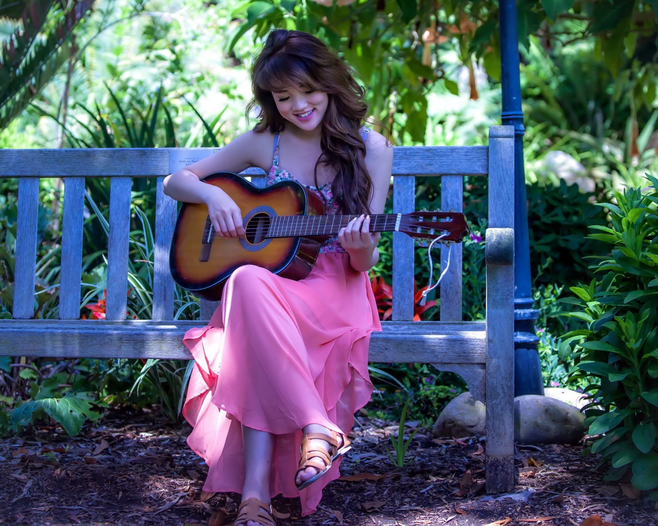 Девушка сидит на скамье в саду и играет на гитаре