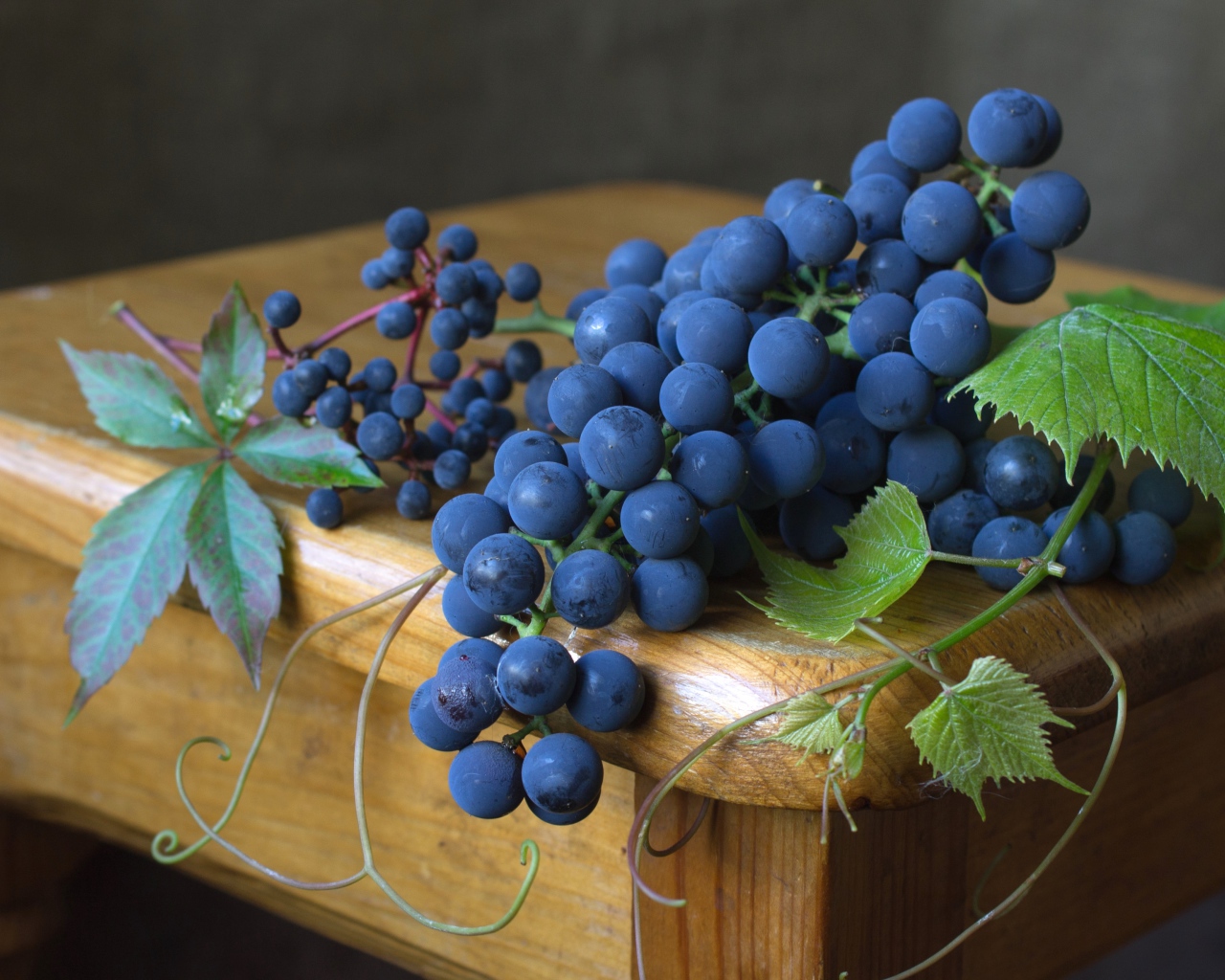 Blue grapes with green leaves lie on a wooden table