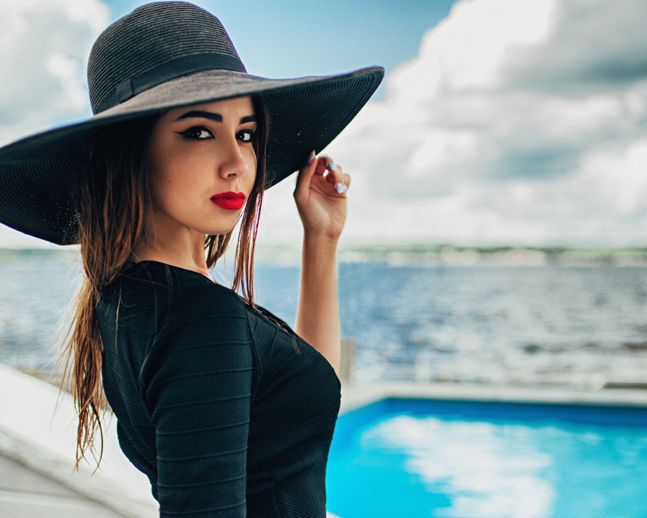 Красивая девушка в большой черной шляпе у бассейна