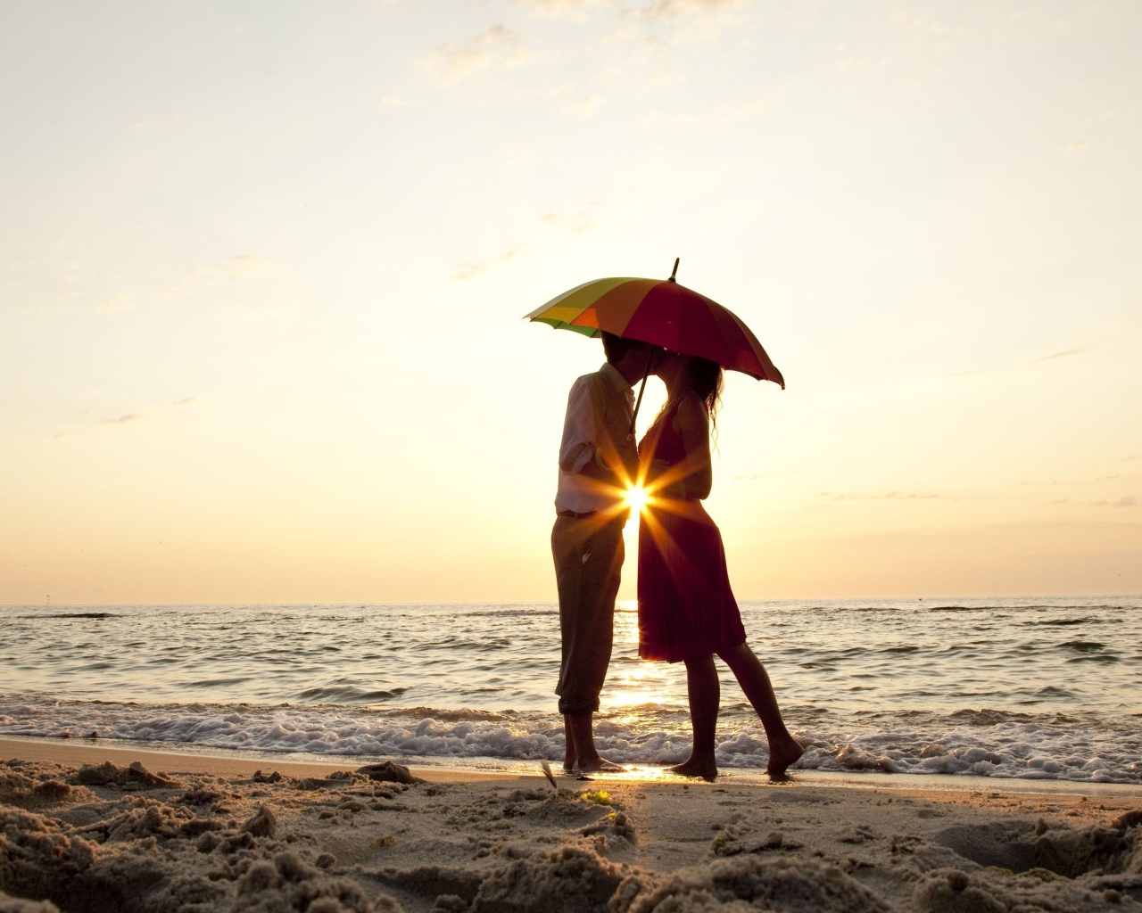 Влюбленная пара на пляже стоит под зонтом на закате
