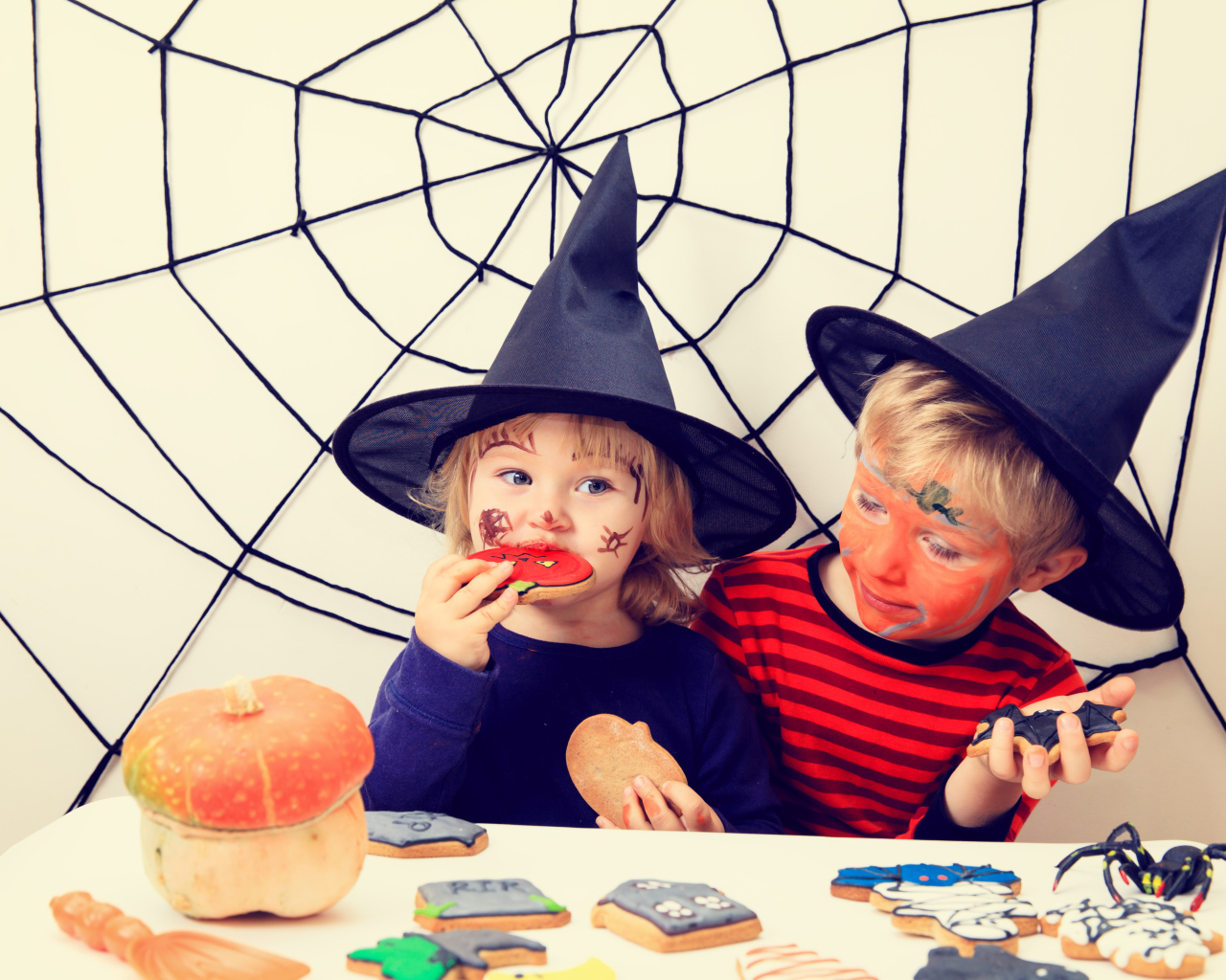 Маленькие дети в костюмах на Хэллоуин едят праздничные сладости