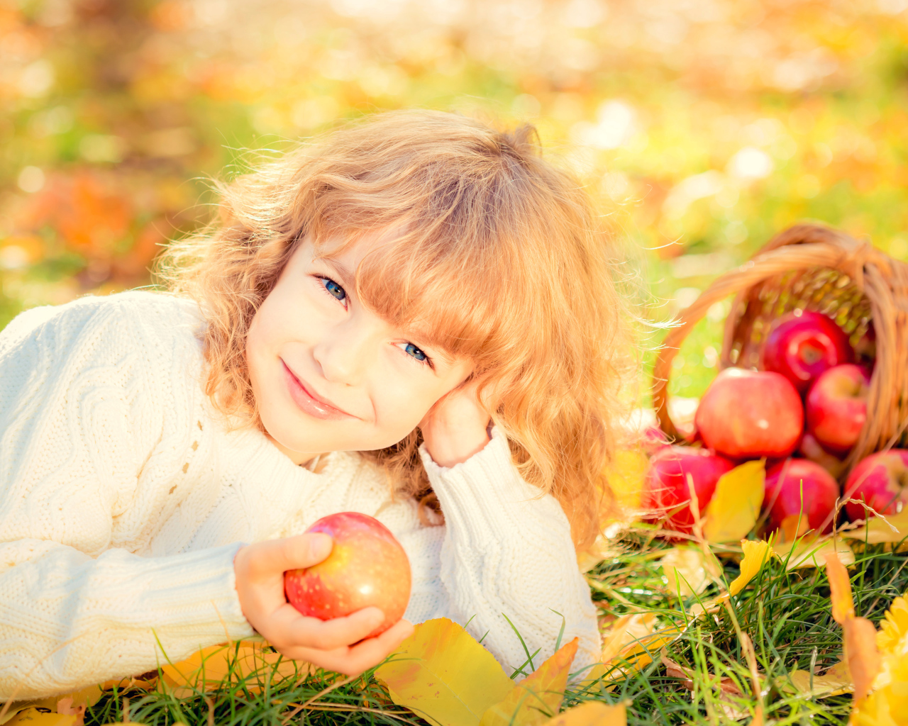 Улыбающаяся рыжеволосая девочка с корзиной красных яблок