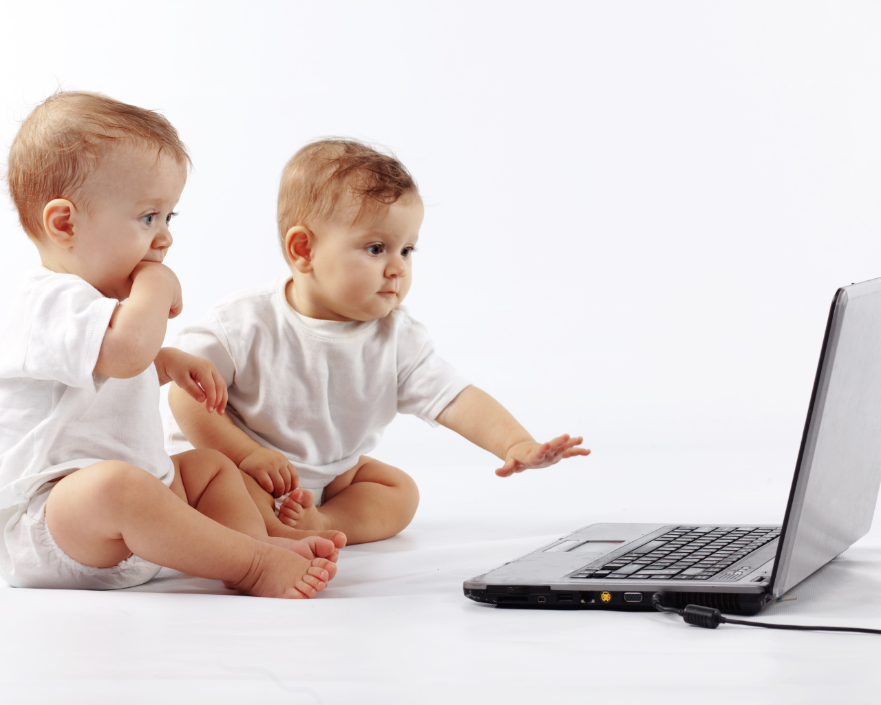Два младенца перед ноутбуком на белом фоне