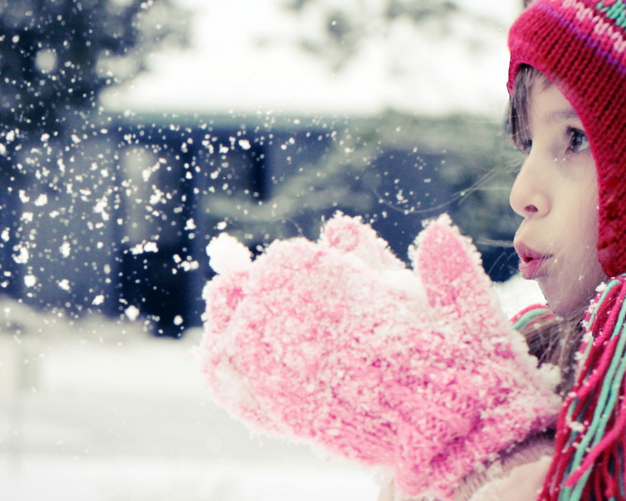 Девочка сдувает белый снег с варежек 