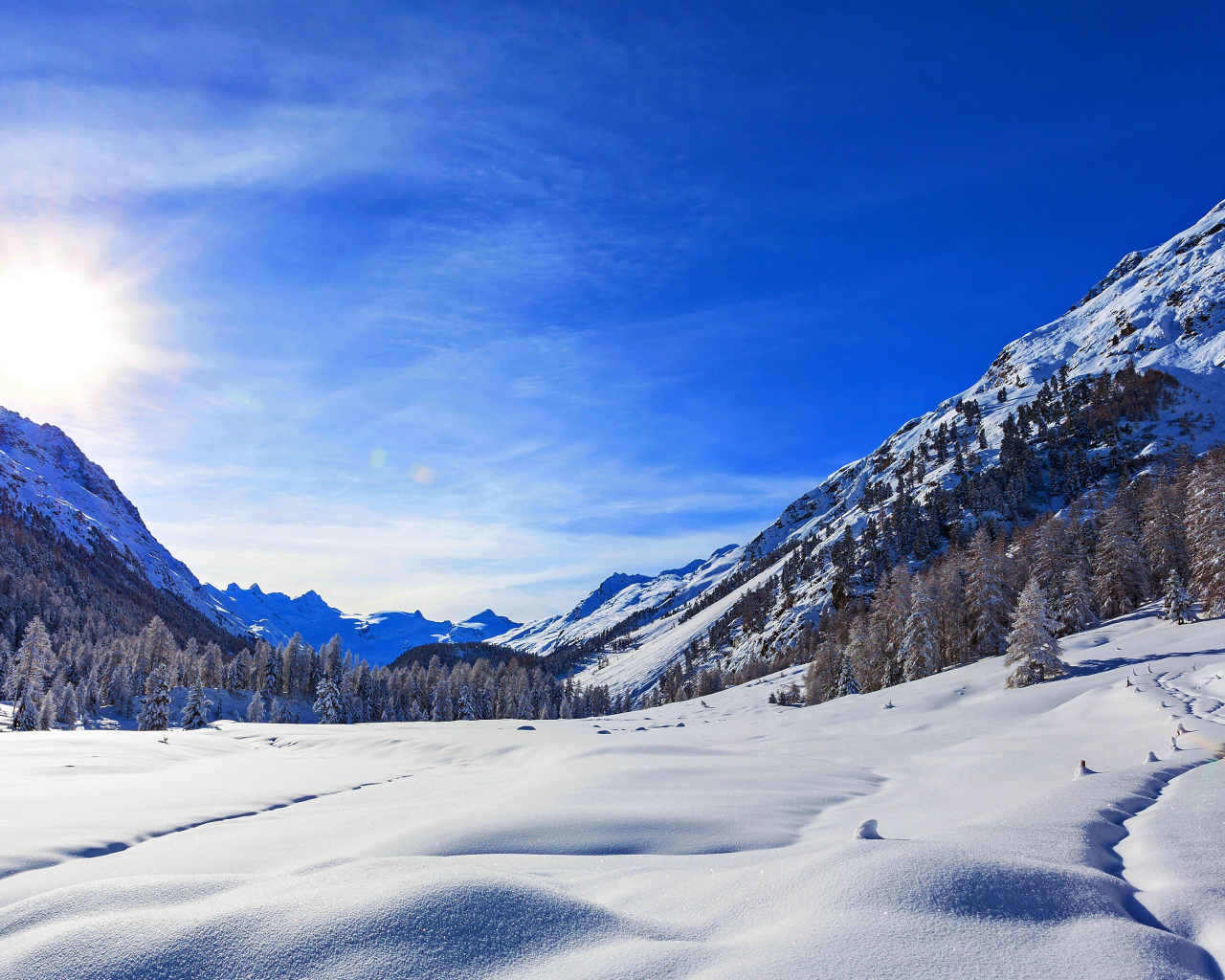 Зимнее солнце в голубом небе над покрытыми снегом горами