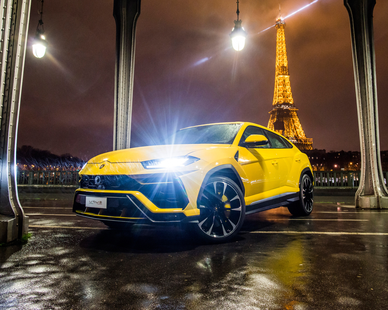Желтый Lamborghini Urus, 2018 с включенными фарами на фоне Эйфелевой башни