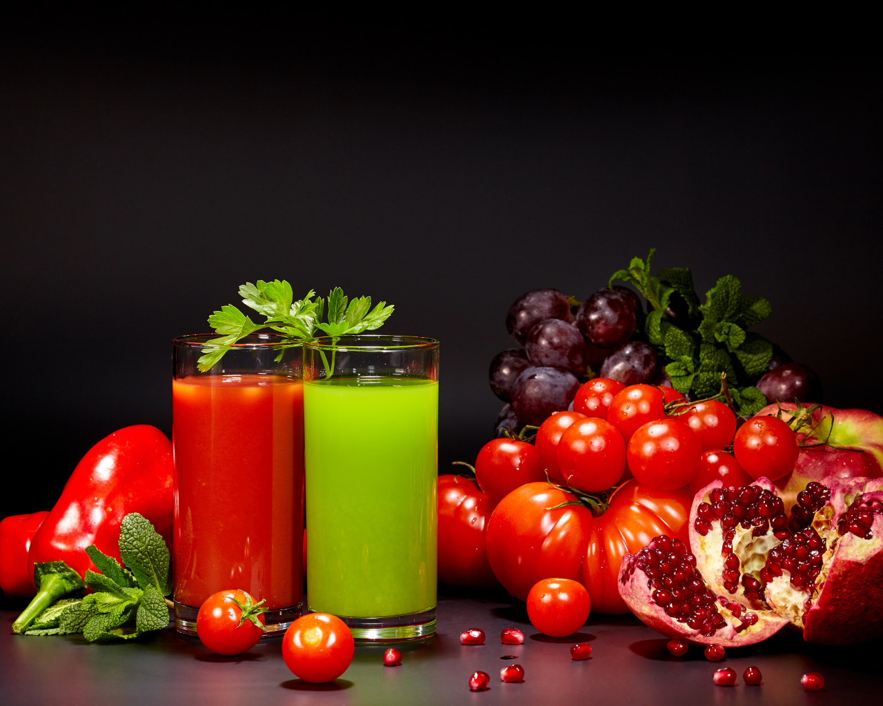 Два стакана сока на столе со свежими помидорами, перцем, гранатом, виноградом и зеленью