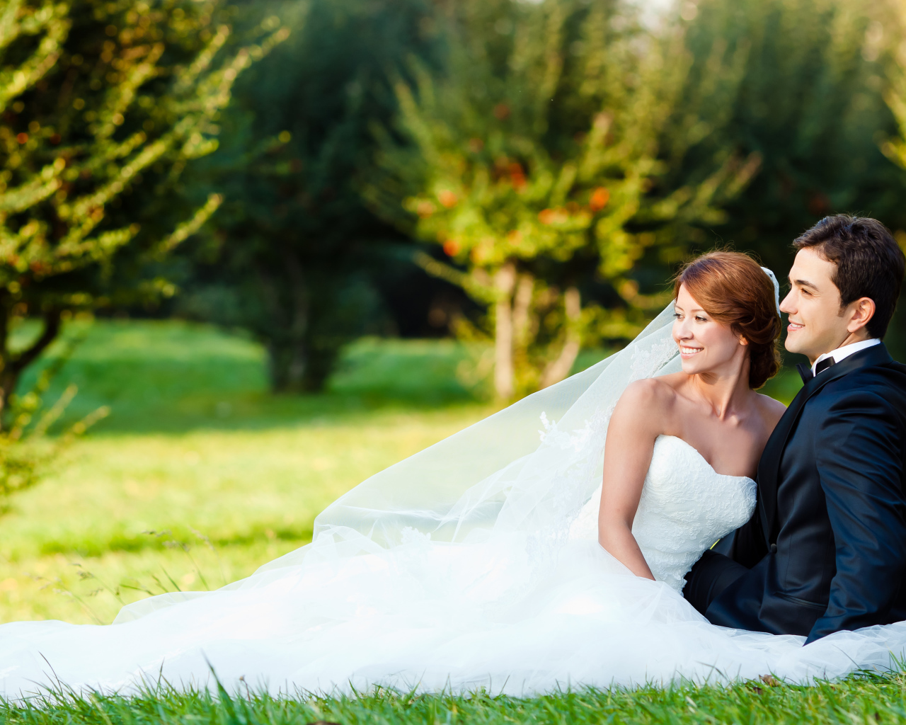 Счастливые жених и невеста сидят на зеленой траве