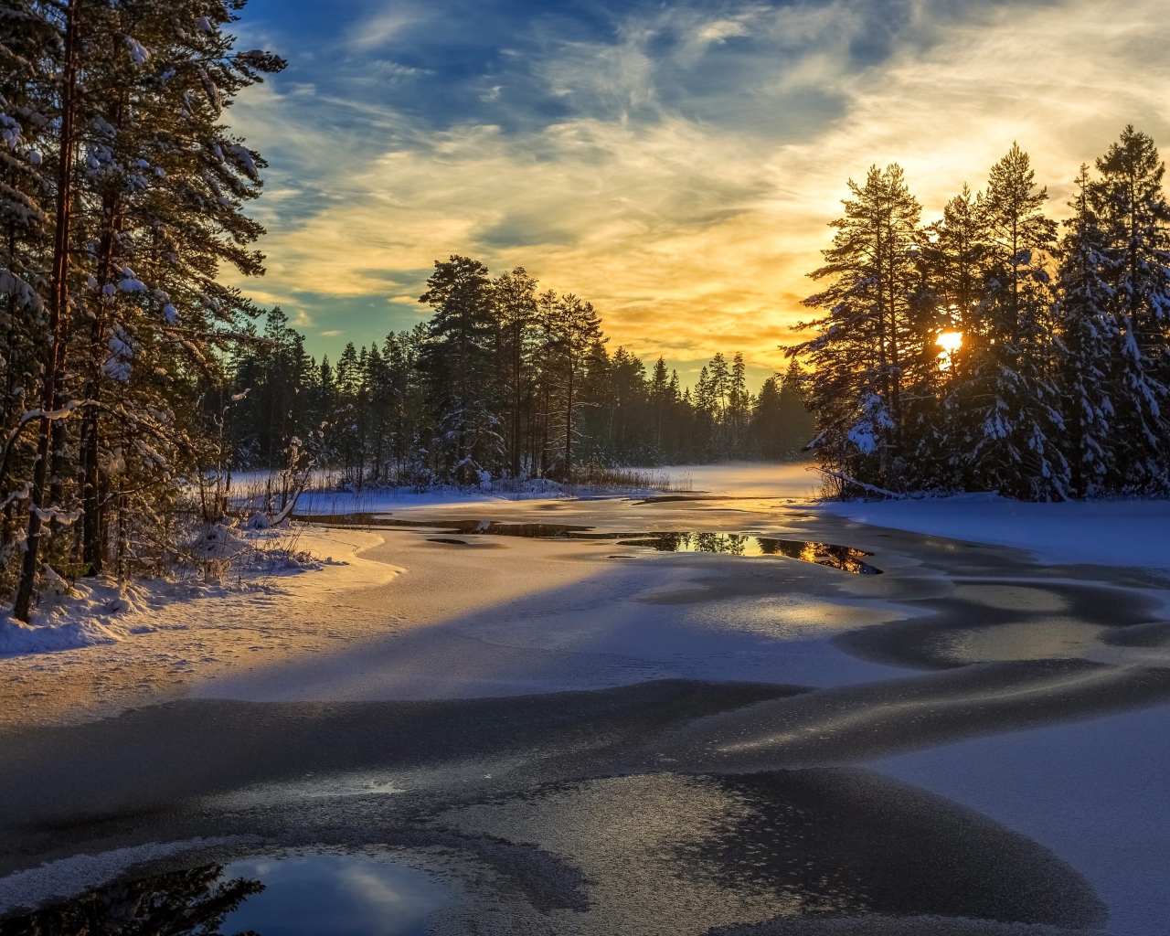 Покрытая льдом река с заснеженными елями по берегам на рассвете