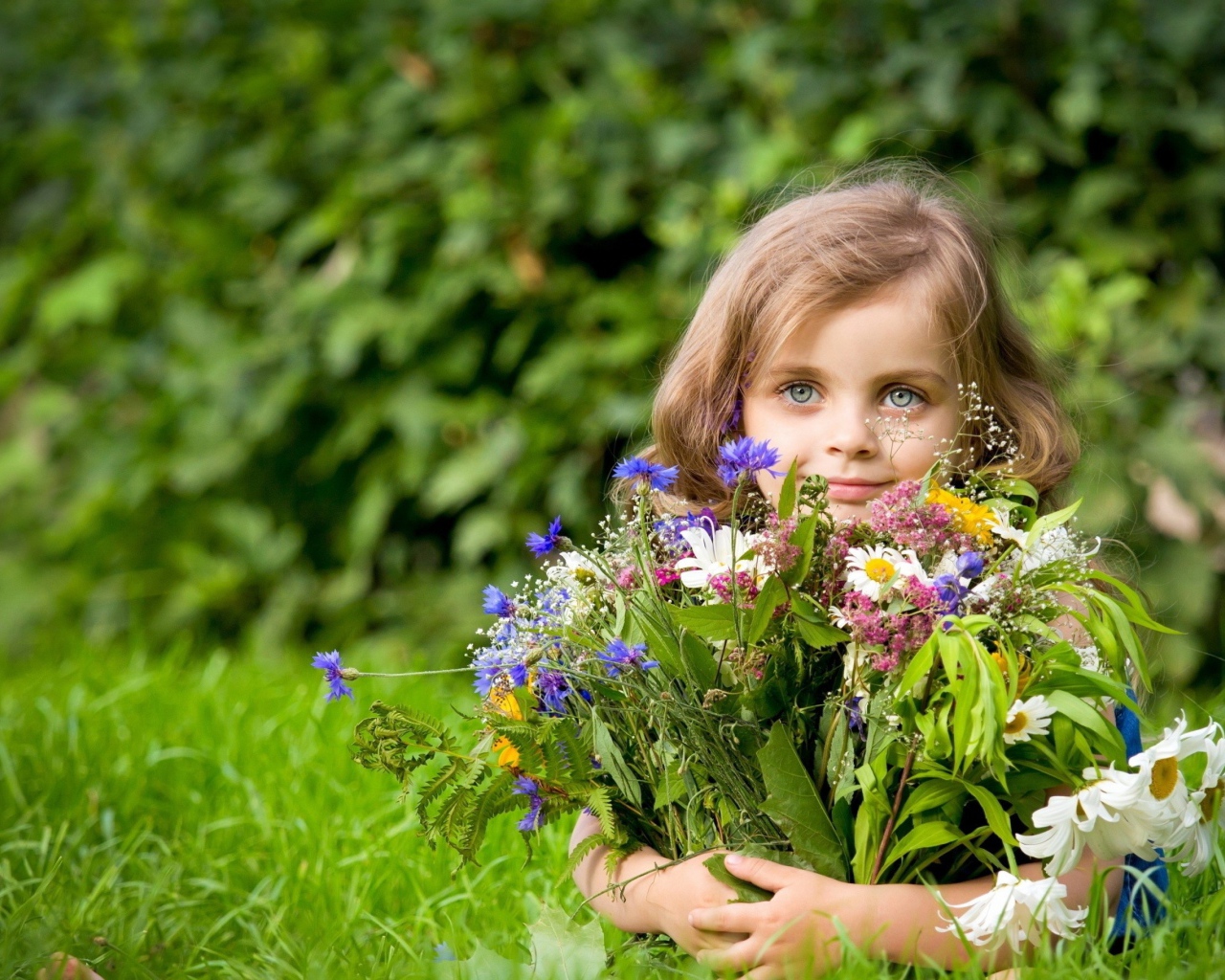 Красивая девочка с букетом цветов лежит на зеленой траве