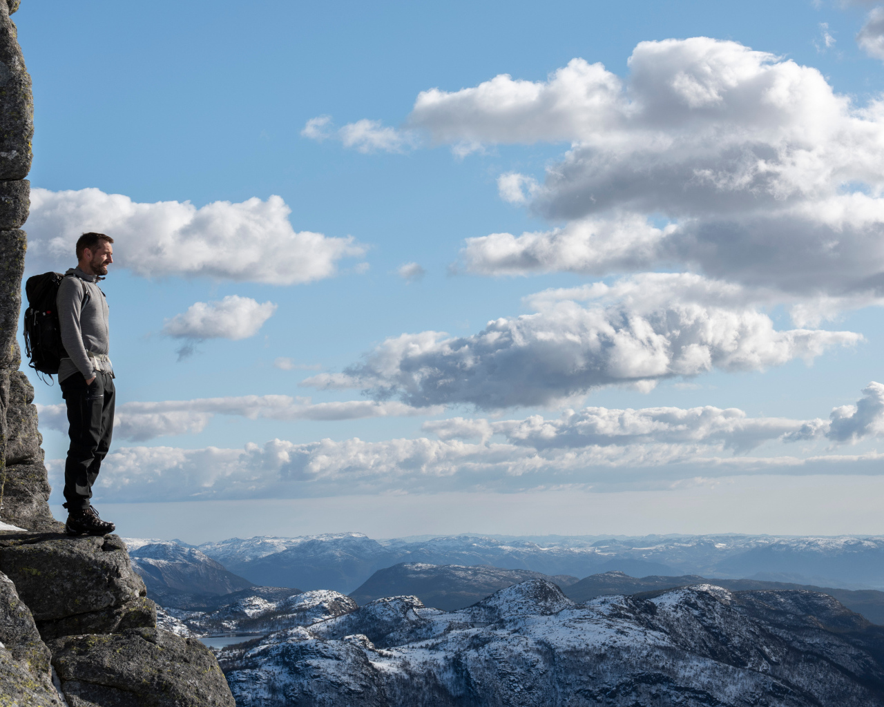 Мужчина стоит на краю скалы на фоне неба 