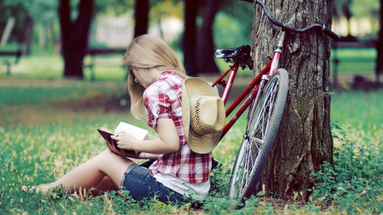 Girl reading a book sitting in a park on the lawn