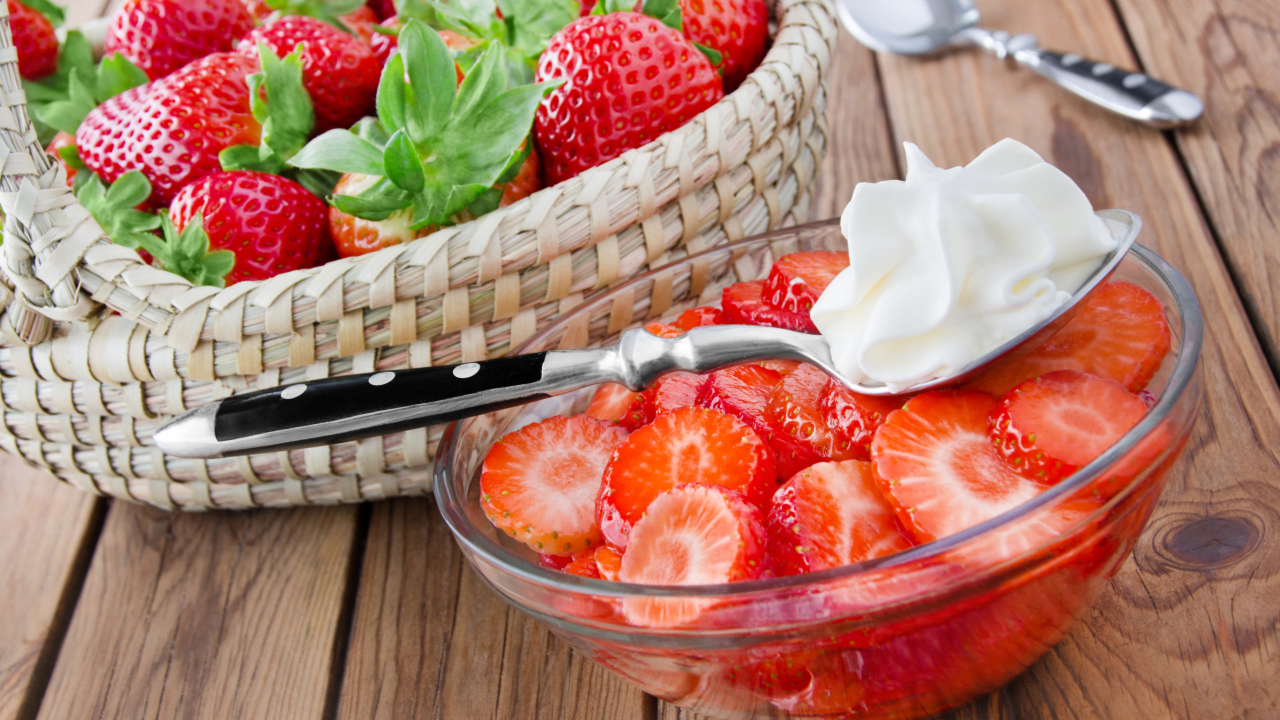 Sliced strawberries in a glass bowl with a spoon of cream