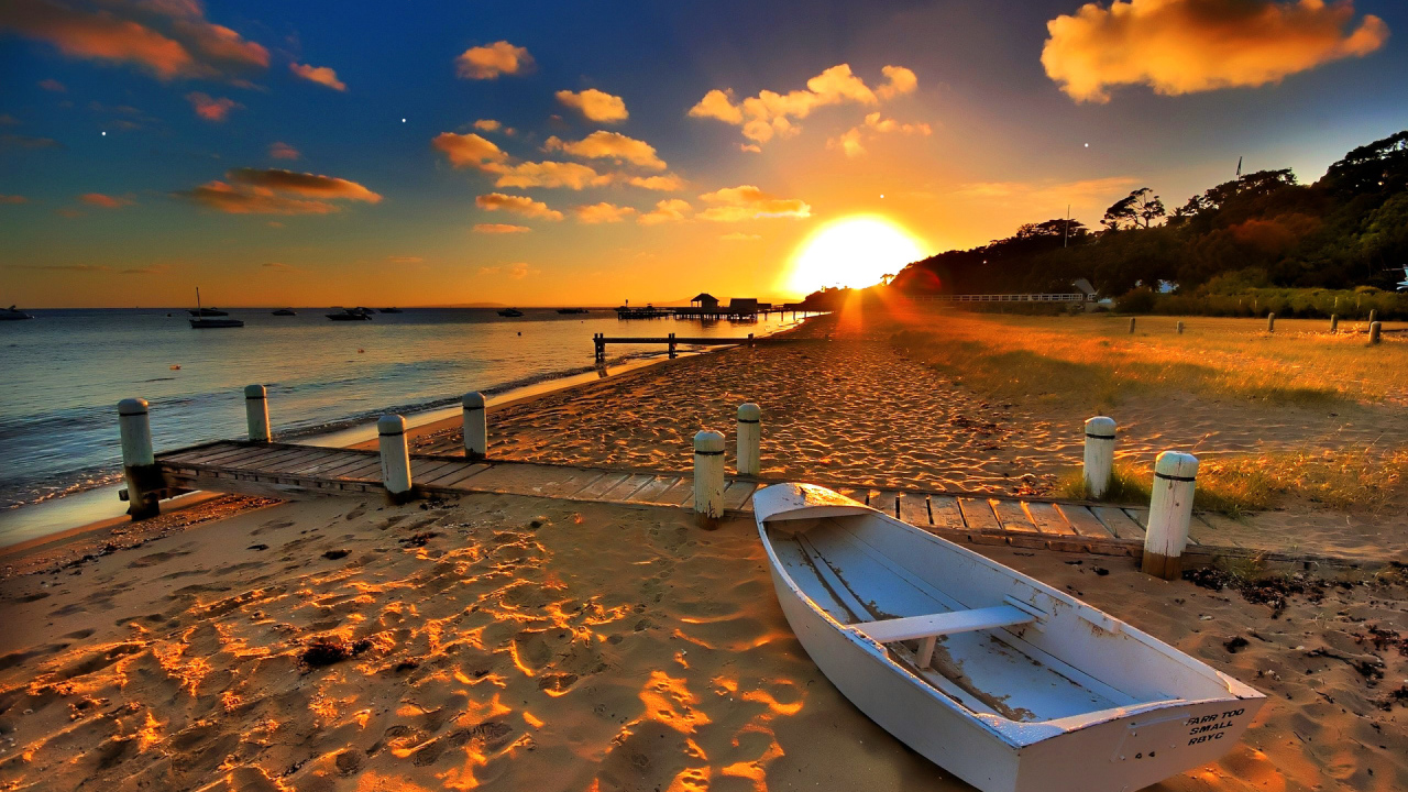Белая лодка на пляже под закатным солнцем