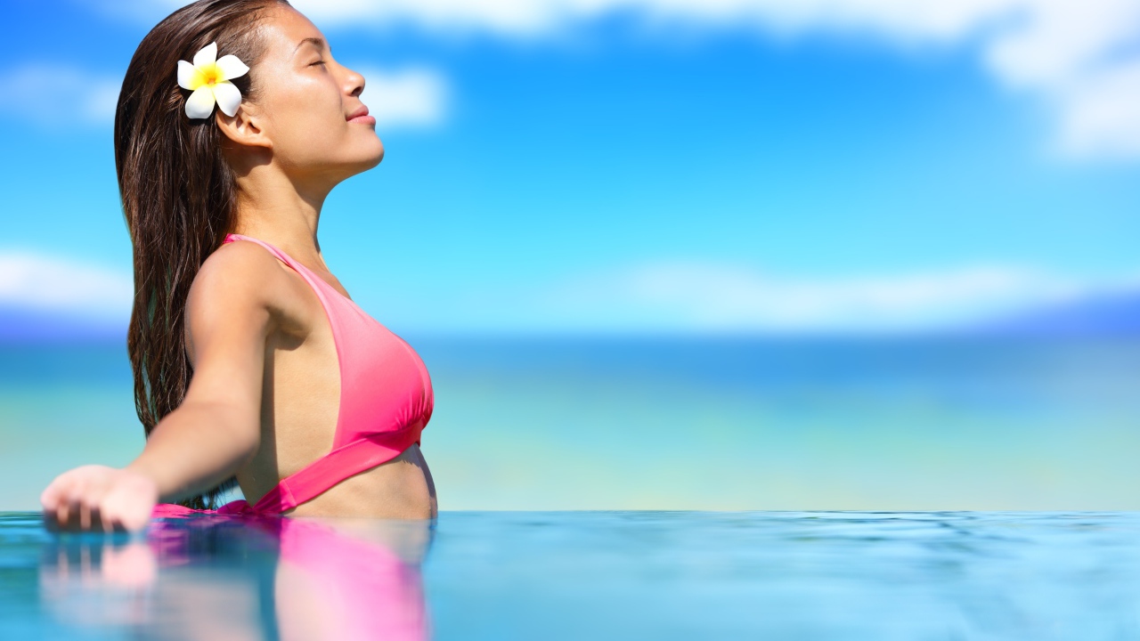 A girl in a pink bathing suit is standing in the water in the sun