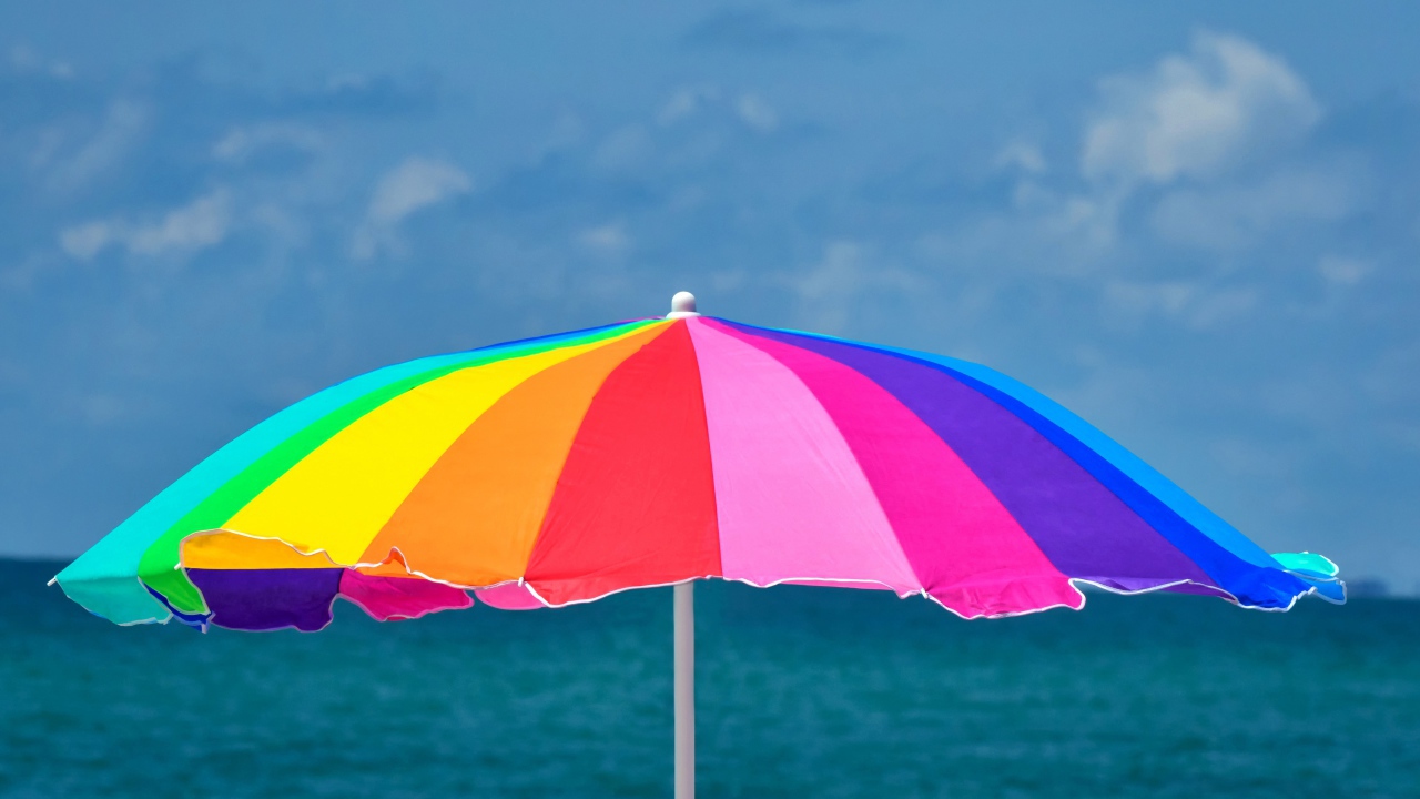 Большой разноцветный пляжный зонт на фоне моря