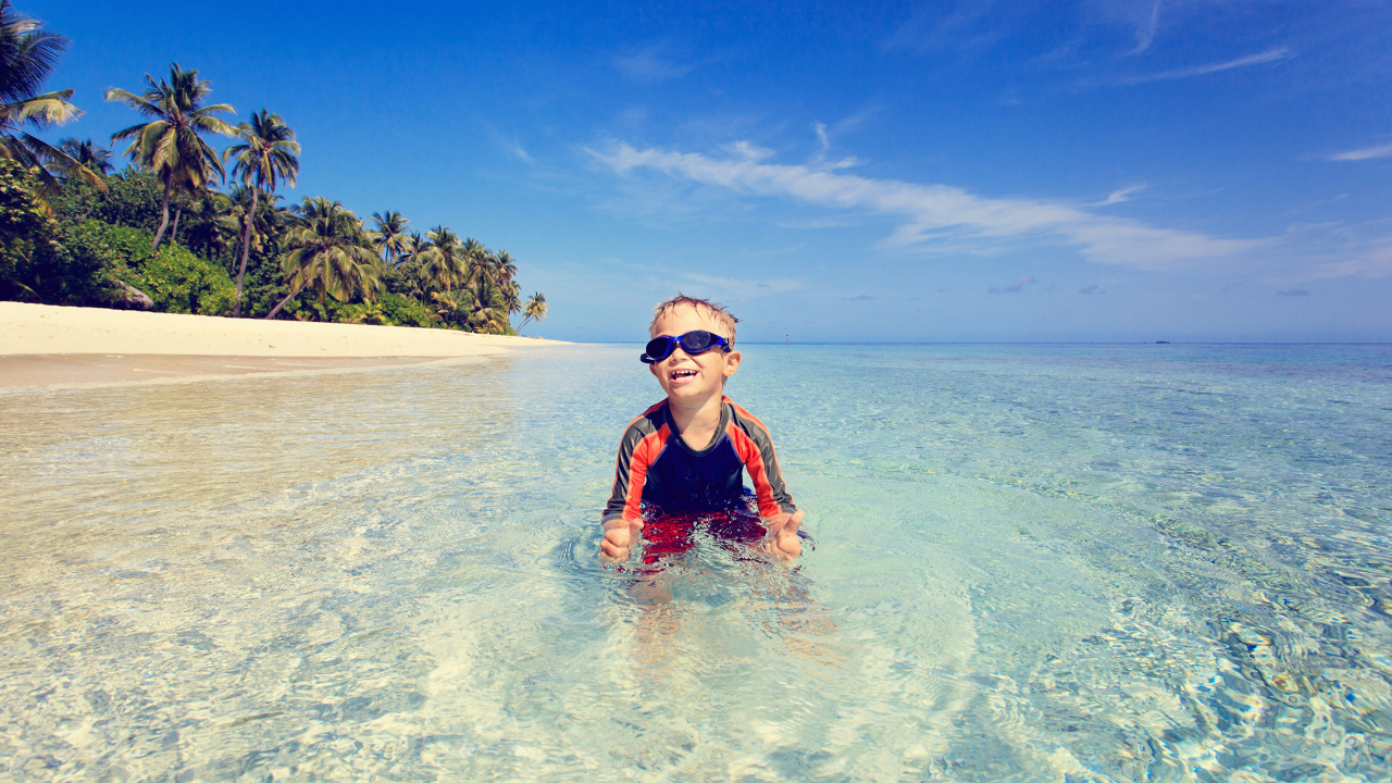 Мальчик в очках сидит в воде на пляже 