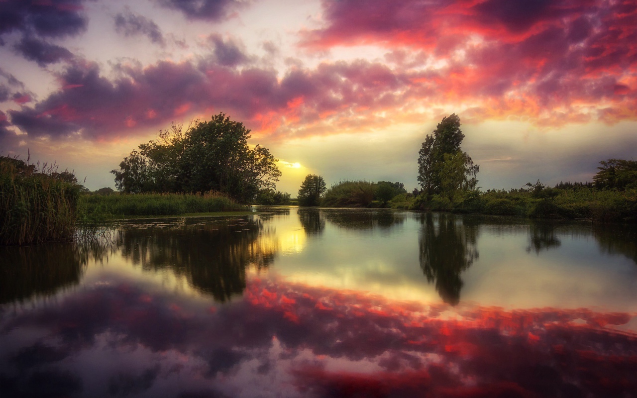 Red clouds are reflected in the clear water of the river