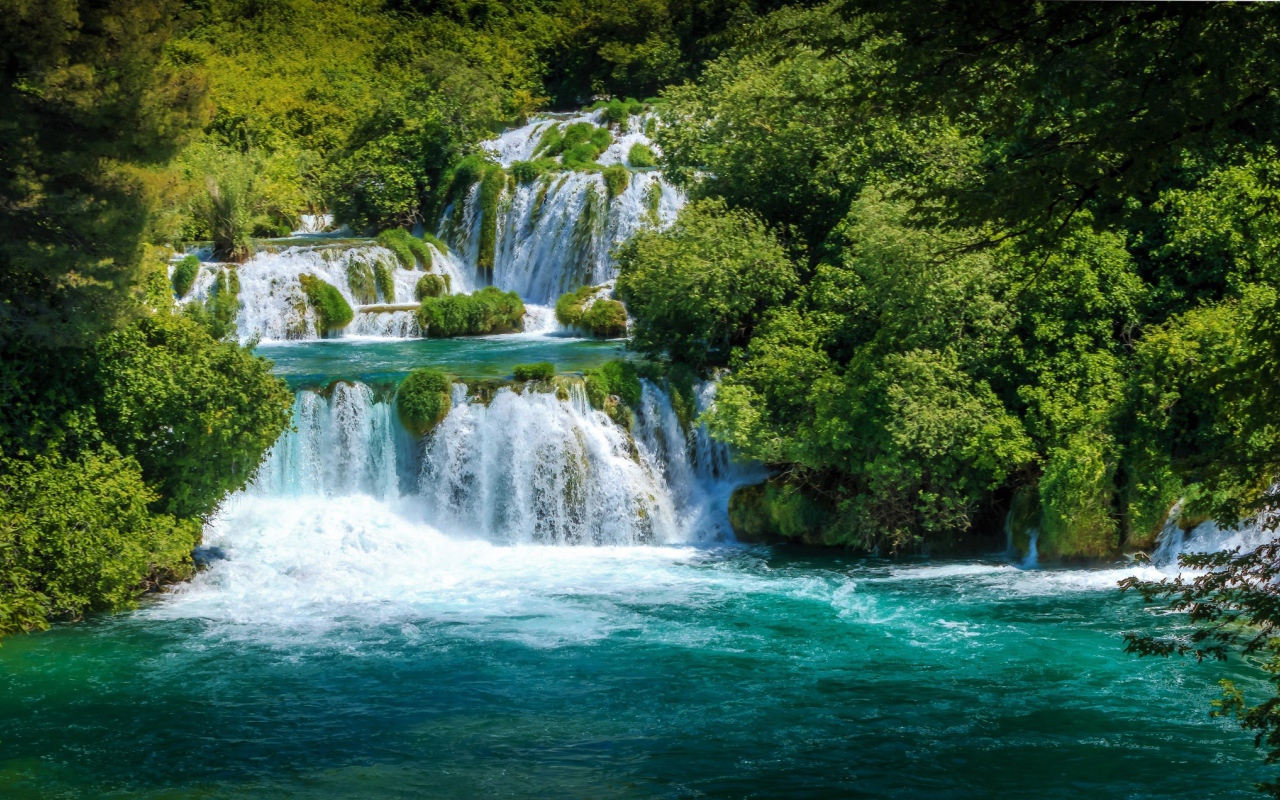 Бушующая голубая вода водопада у зеленых деревьев