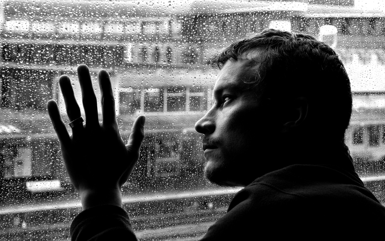 Грустный мужчина стоит у мокрого окна 