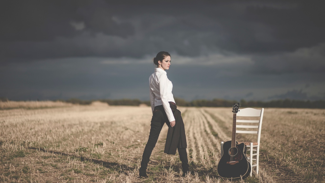 Девушка в поле у стула с гитарой