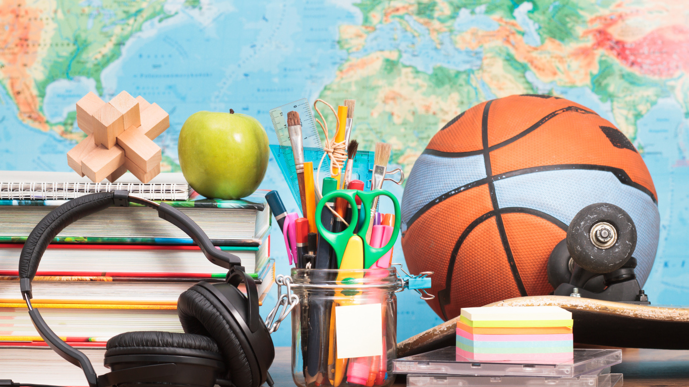 Мяч, наушники, книги и канцелярские принадлежности на столе на фоне карты