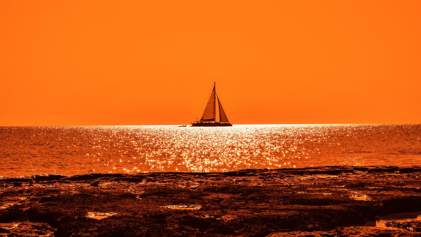 Парусная лодка на горизонте в океане на закате солнца