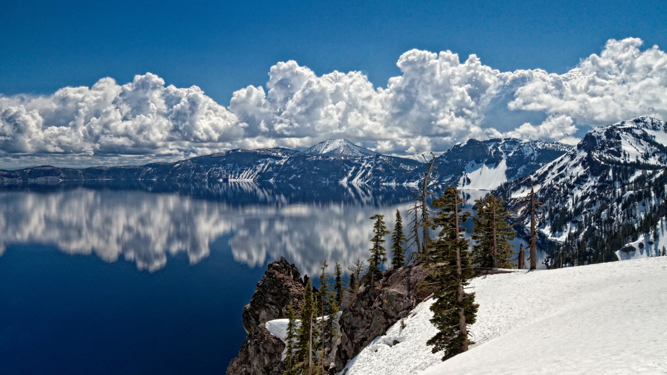 Белые облака отражаются в чистой воде озера у горного хребта