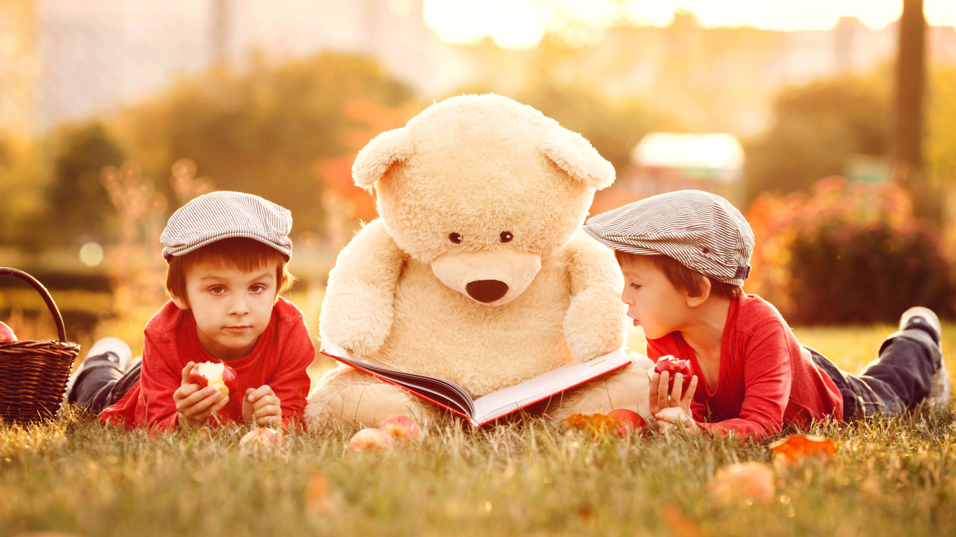 Большой плюшевый медведь с книгой и маленькие мальчики лежат на зеленой траве 