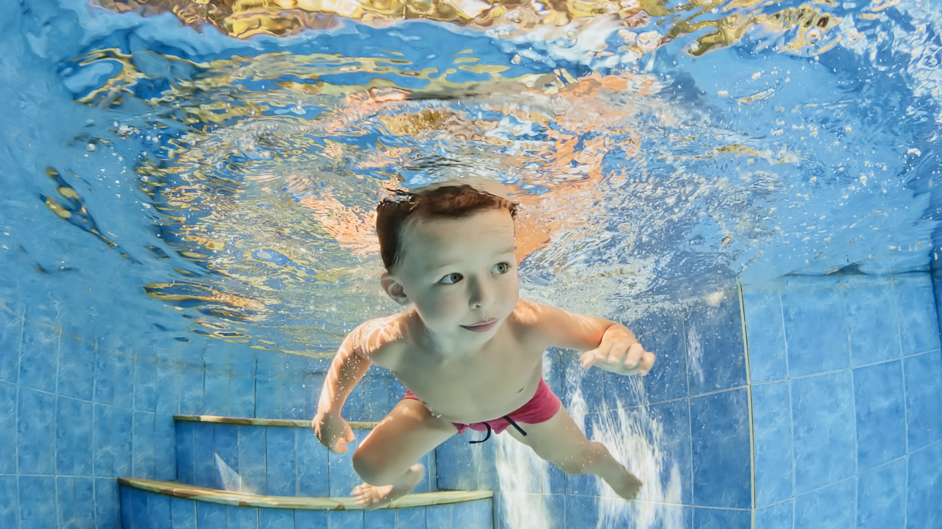 Маленький мальчик плавает под водой в бассейне