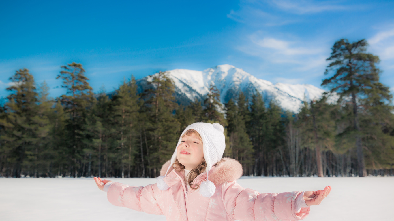 Маленькая девочка в розовой куртке на фоне гор зимой