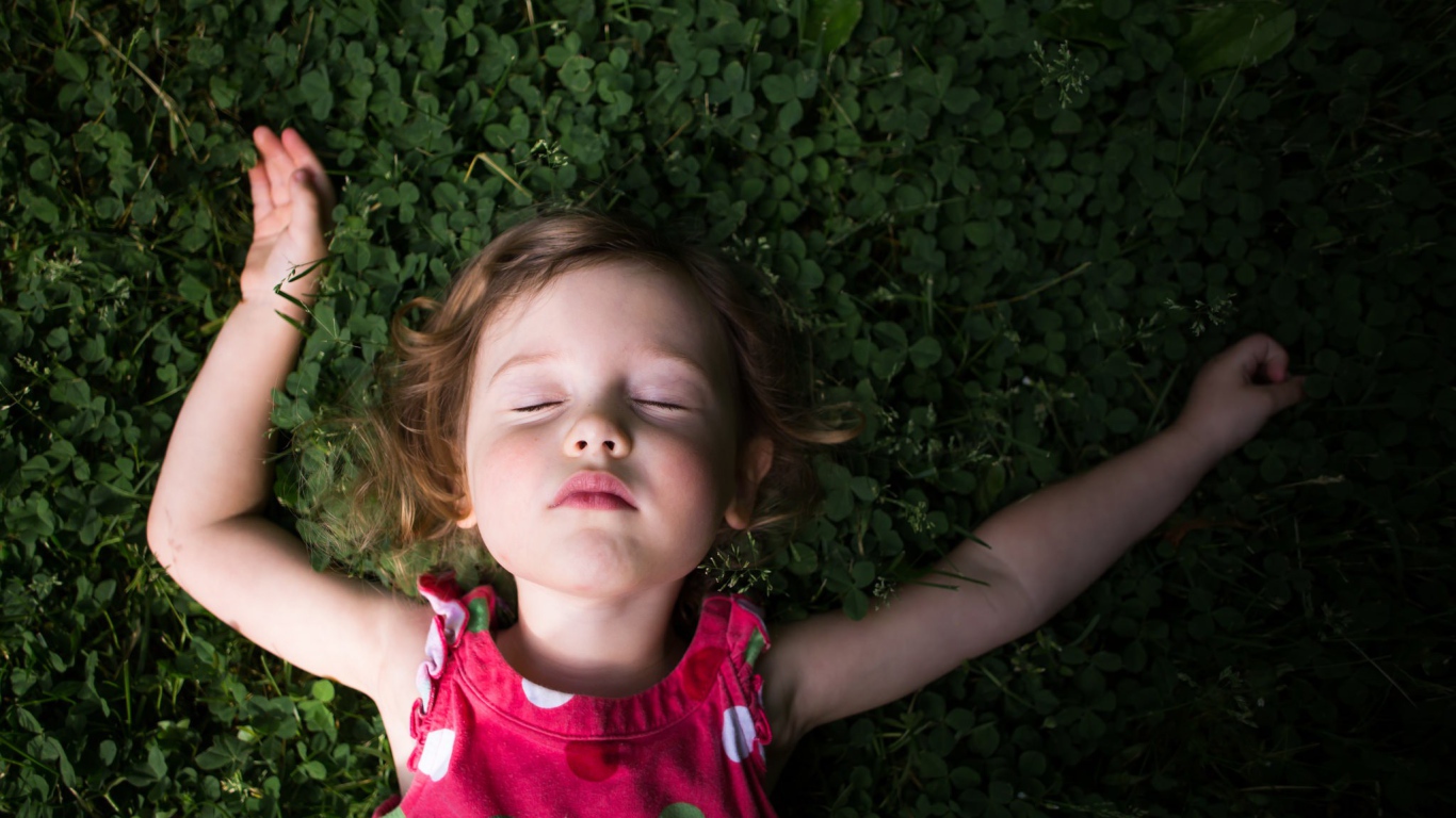 Маленькая девочка спит на зеленой траве 