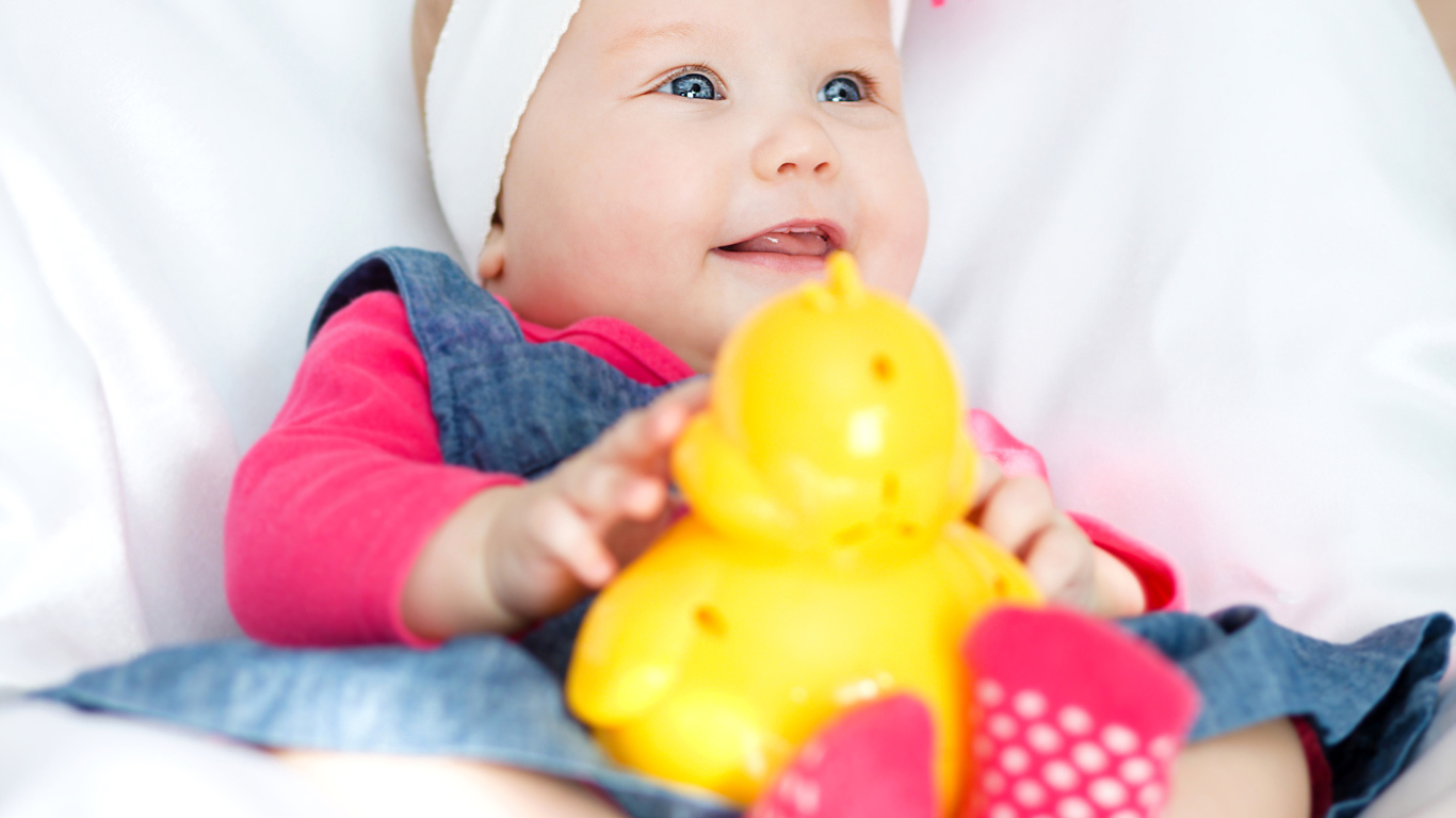 Smiling blue-eyed baby girl with toy in hands