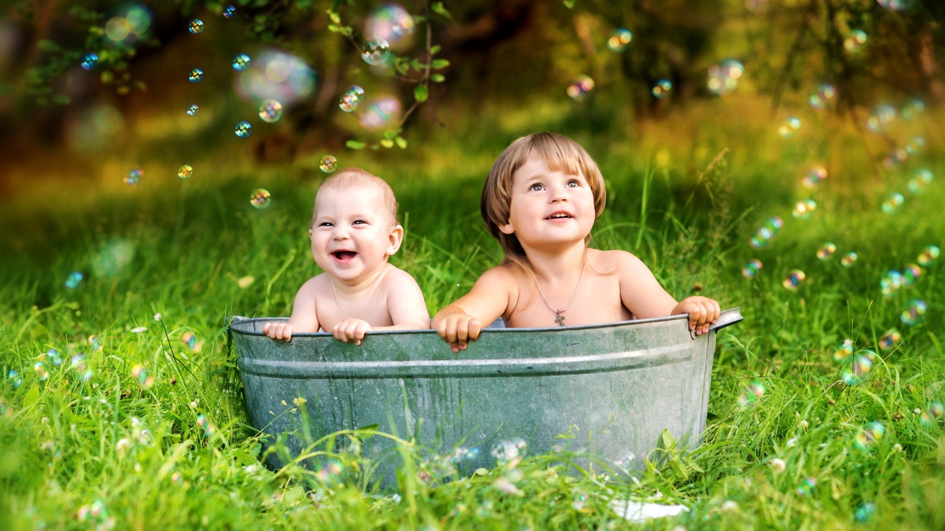 Два маленьких ребенка сидят в железном корыте на зеленой траве
