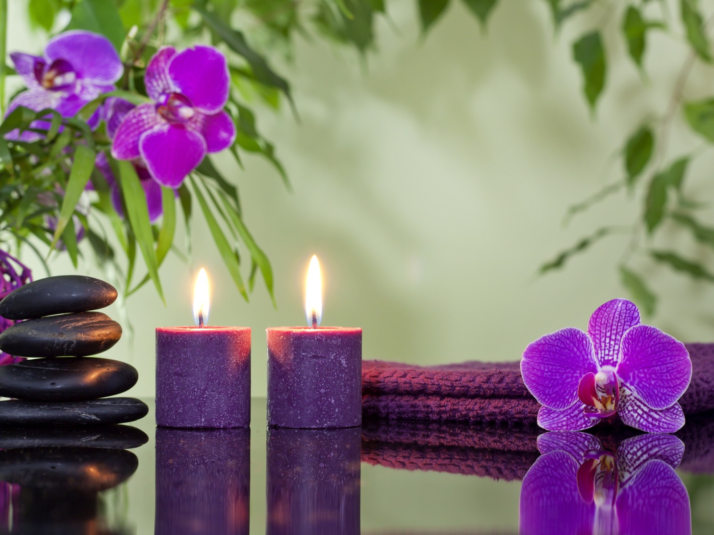 Две горящие свечи с камнями и цветами орхидеи отражаются в зеркальной поверхности стола