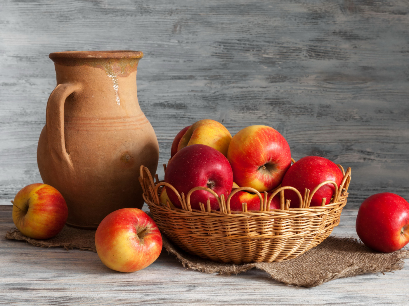 Красные яблоки в корзинке на столе с кувшином