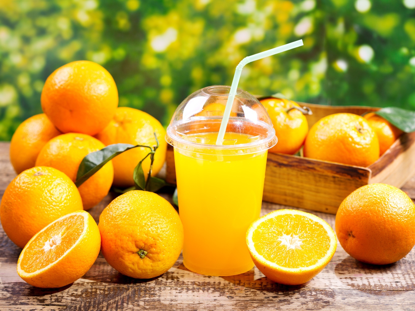 Стакан апельсинового сока с трубочкой на столе со свежими апельсинами