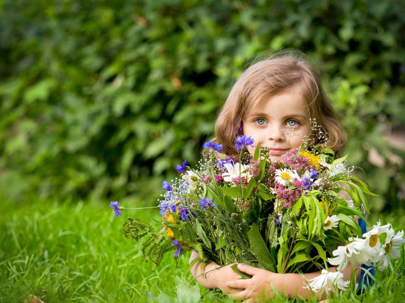 Beautiful girl with a bouquet of flowers lies on a green grass