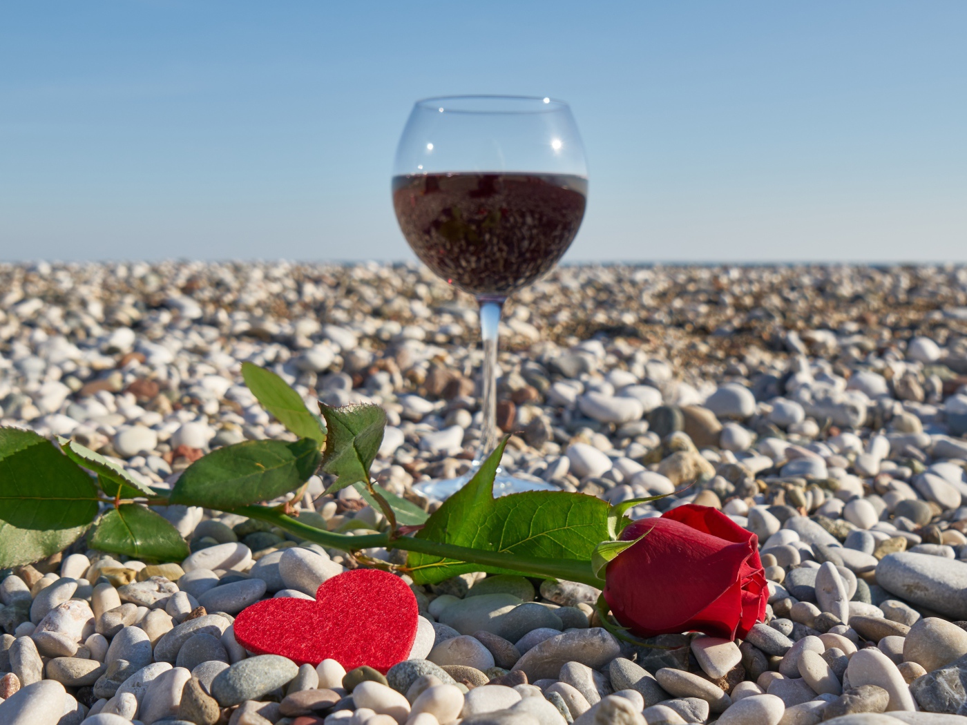 Красная роза на морской гальке с сердечком и бокалом вина