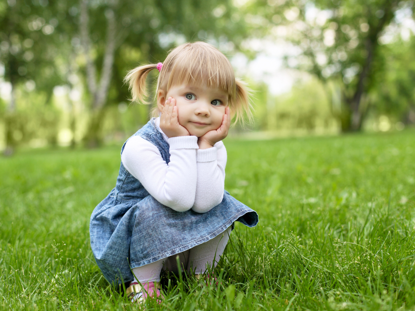 Маленькая девочка в сарафане сидит на траве 