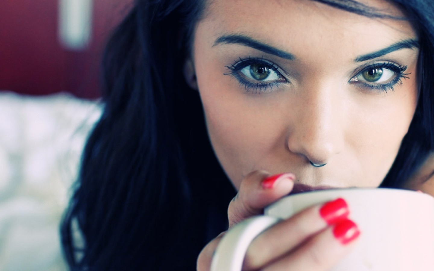 Девушка брюнетка с пирсингом в носу и красными ногтями